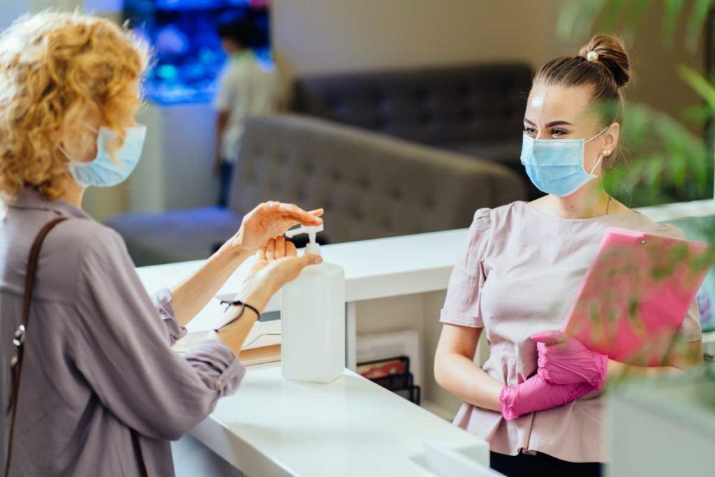 Woman Washing Hands With Alcohol Gel At Reception Counter